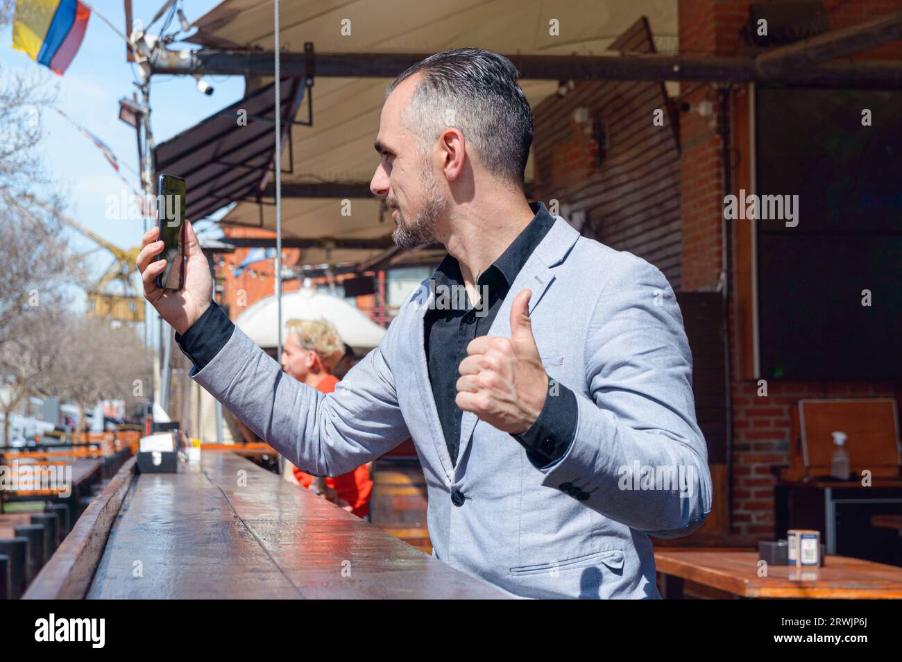 Homme d'affaires adulte caucasien assis à l'extérieur du restaurant sur un comptoir en bois, content de regarder son téléphone en attendant la serveuse Banque D'Images