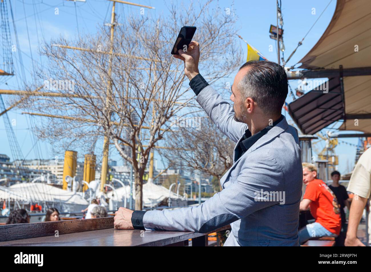 Homme d'affaires adulte caucasien dans une veste de costume élégante prenant selfie avec son téléphone assis à l'extérieur du restaurant, concept de technologie, espace de copie. Banque D'Images