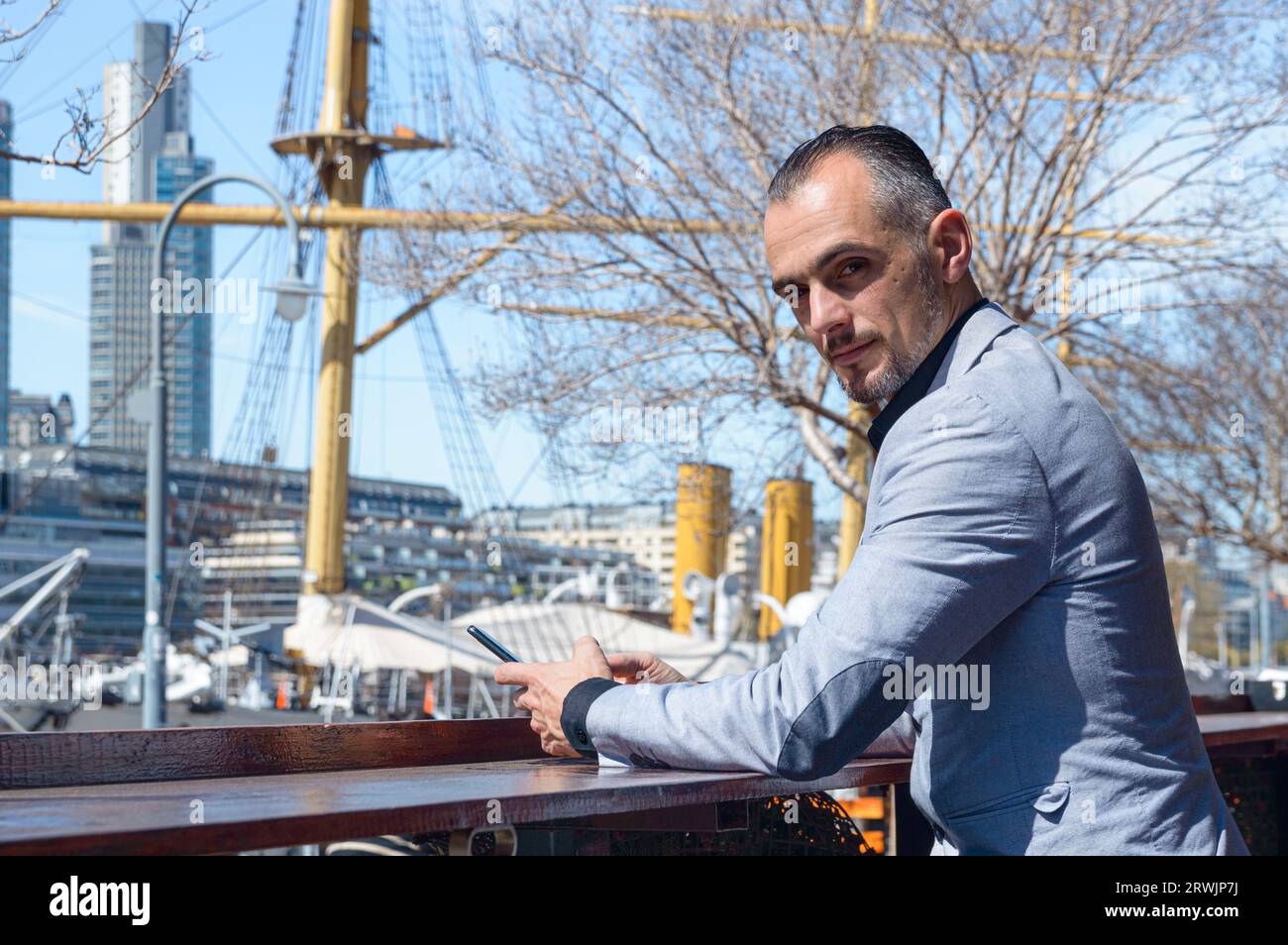 homme adulte caucasien élégant, entrepreneur d'affaires assis à l'extérieur du restaurant avec le téléphone dans la main tournant regardant la caméra et souriant Banque D'Images