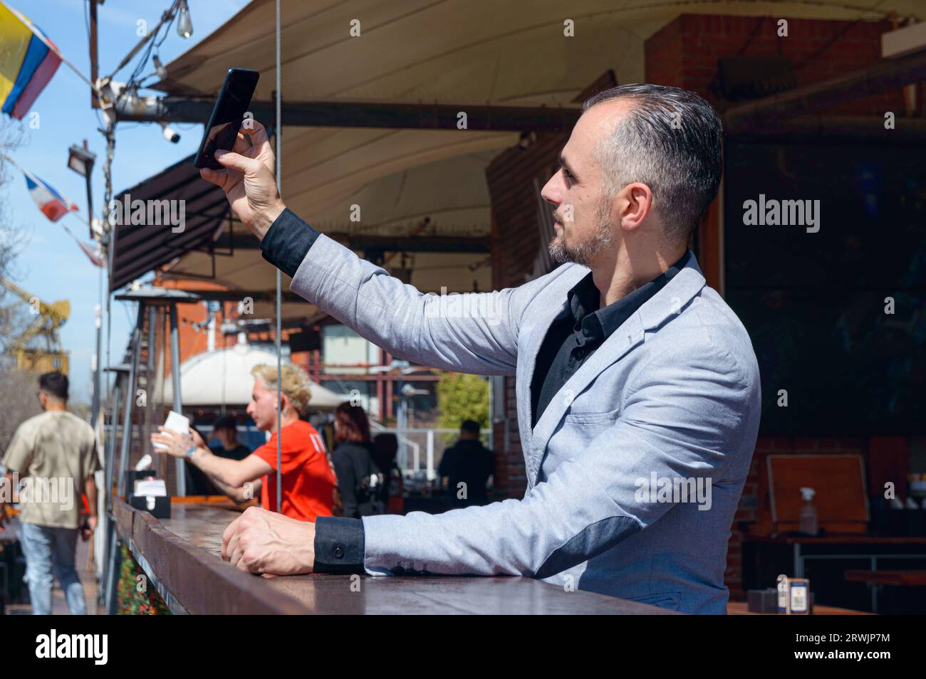 Homme d'affaires adulte caucasien dans une veste de costume élégante prenant selfie avec son téléphone assis à l'extérieur du restaurant, concept de technologie, espace de copie. Banque D'Images