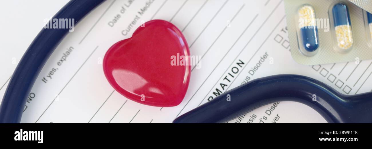 Cœur rouge, stéthoscope et pilules sur la feuille des antécédents médicaux du patient. Banque D'Images