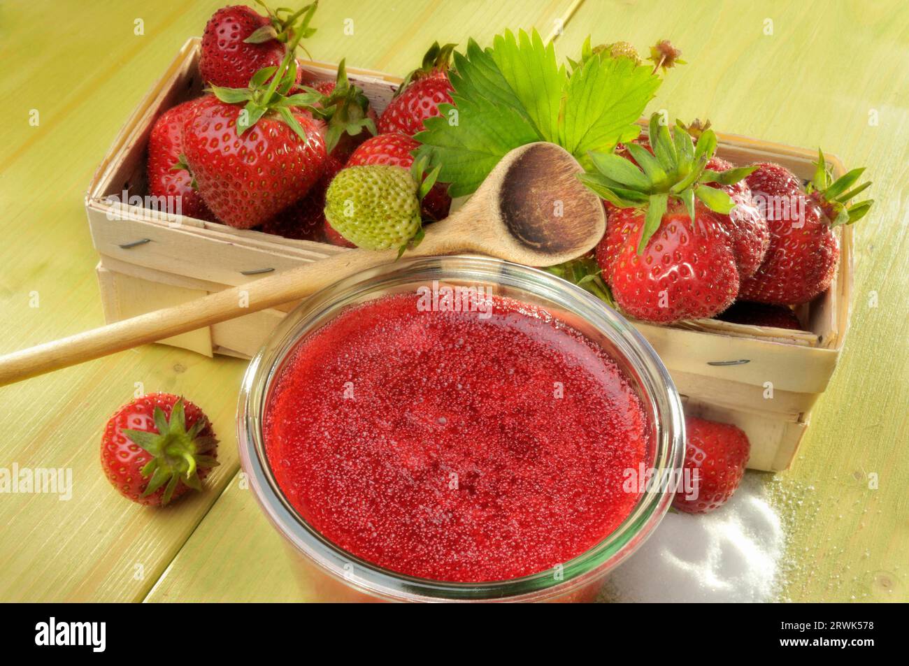 Confiture de fraises maison dans un bocal à côté d'un panier de fraises fraîches, cuillère de cuisson et sucre Banque D'Images