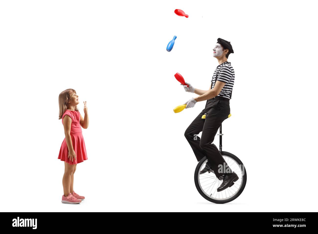 Petite fille regardant avec amusement un mime chevauchant un monocycle et jonglant isolé sur fond blanc Banque D'Images