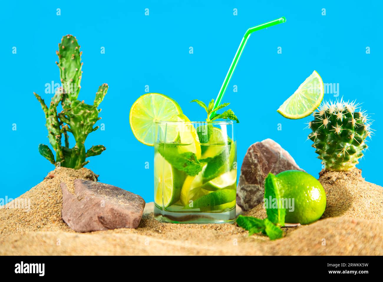 Verre de limonade à la chaux et à la menthe parmi les dunes de sable et les cactus. Fond bleu. Banque D'Images