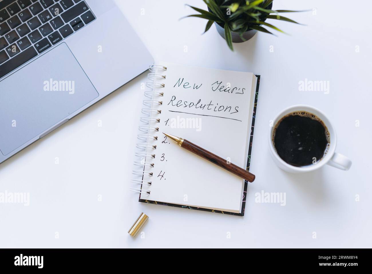 ouvrez le bloc-notes avec le texte des résolutions du nouvel an. et liste vide. Fleur, ordinateur portable et tasse à café sur fond. Banque D'Images