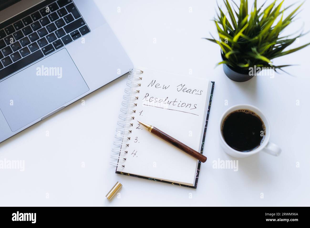 ouvrez le bloc-notes avec le texte des résolutions du nouvel an. et liste vide. Fleur, ordinateur portable et tasse à café sur fond. Banque D'Images
