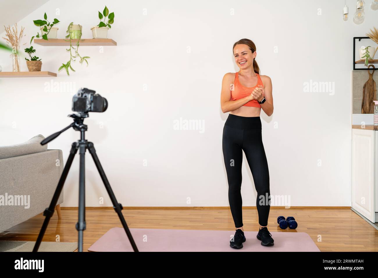 Jeune femme sportive entraîneur de fitness portant des vêtements de sport debout devant la caméra sur trépied et enregistrant son blog vidéo sur un mode de vie sain. Banque D'Images