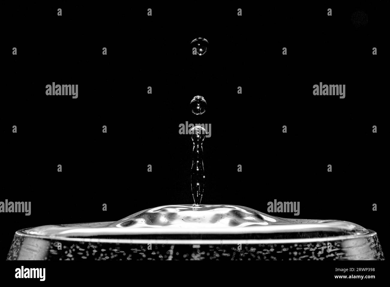 Gouttes d'eau réfléchissantes émergeant d'un verre d'eau devant un fond noir. Banque D'Images