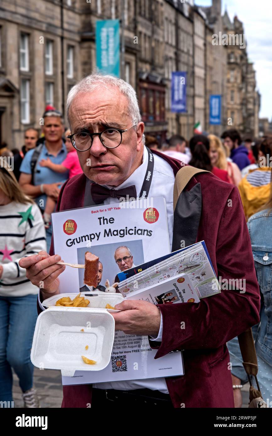 Un magicien grincheux faisant la promotion de son spectacle de franges d'Édimbourg et mangeant un souper de saucisses sur la High Street, Édimbourg, Écosse, Royaume-Uni. Banque D'Images