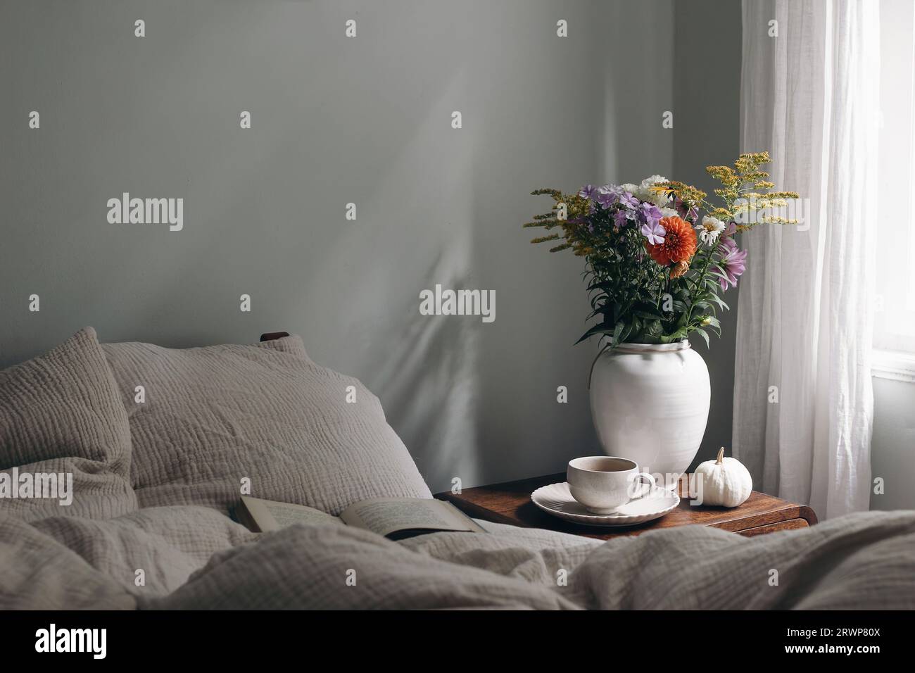 Intérieur élégant de la chambre moody. Tasse de café, citrouille sur table de chevet en bois rétro. Vase en céramique blanche. Bouquet de dahlia, cosmos, fleurs de solidago Banque D'Images