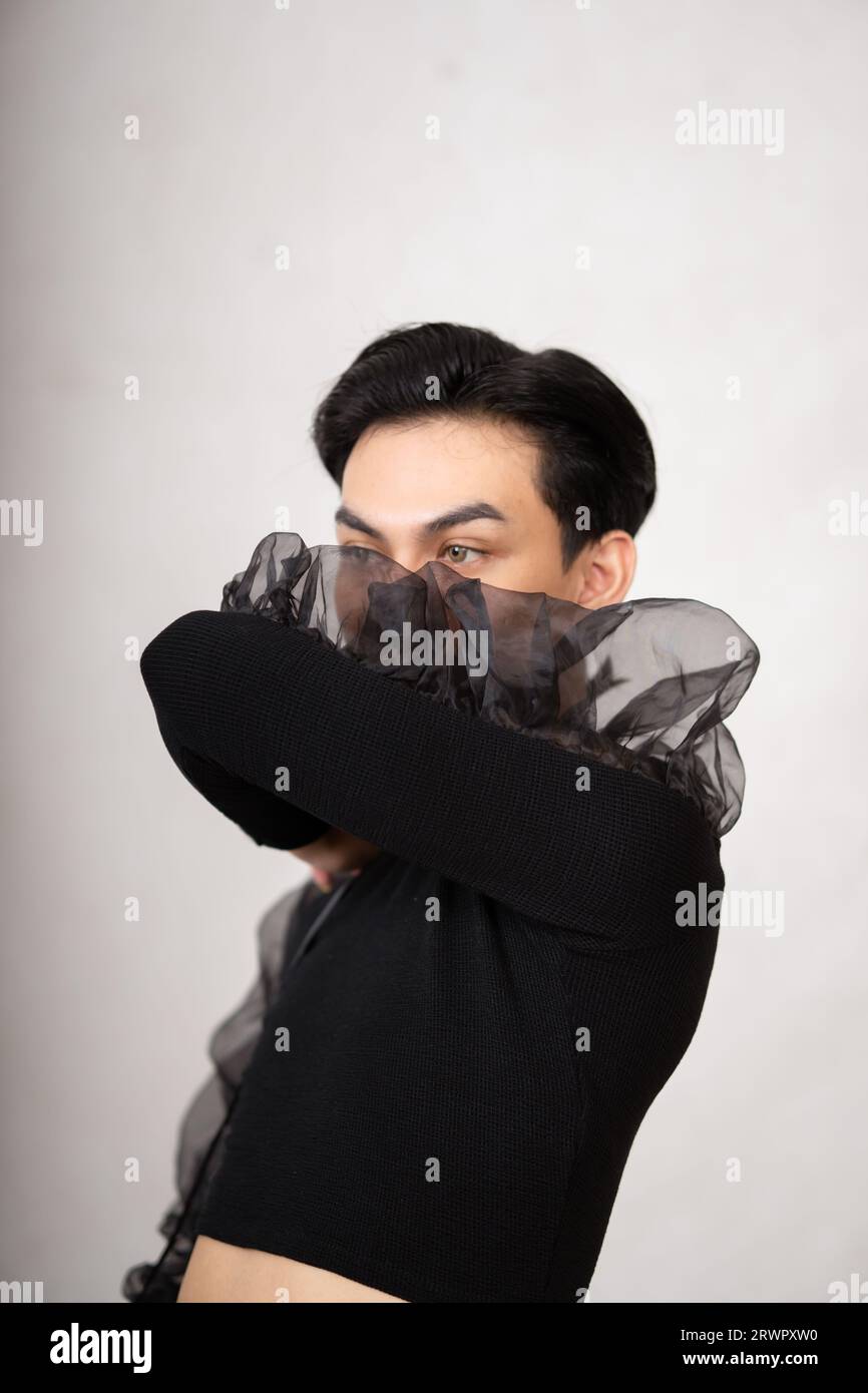 Homme asiatique avec un joli visage portant un costume noir tout en posant à l'intérieur de la salle blanche au studio Banque D'Images
