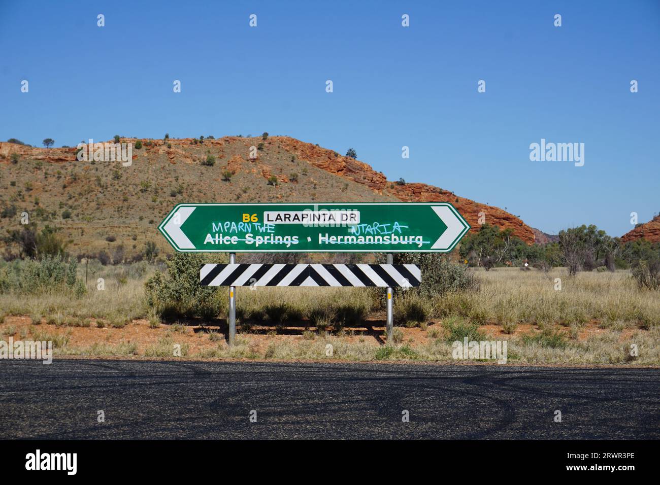 Panneau routier avec noms anglais barré et remplacé par des noms aborigènes avec graffiti près d'Alice Springs, territoire du Nord, Australie Banque D'Images