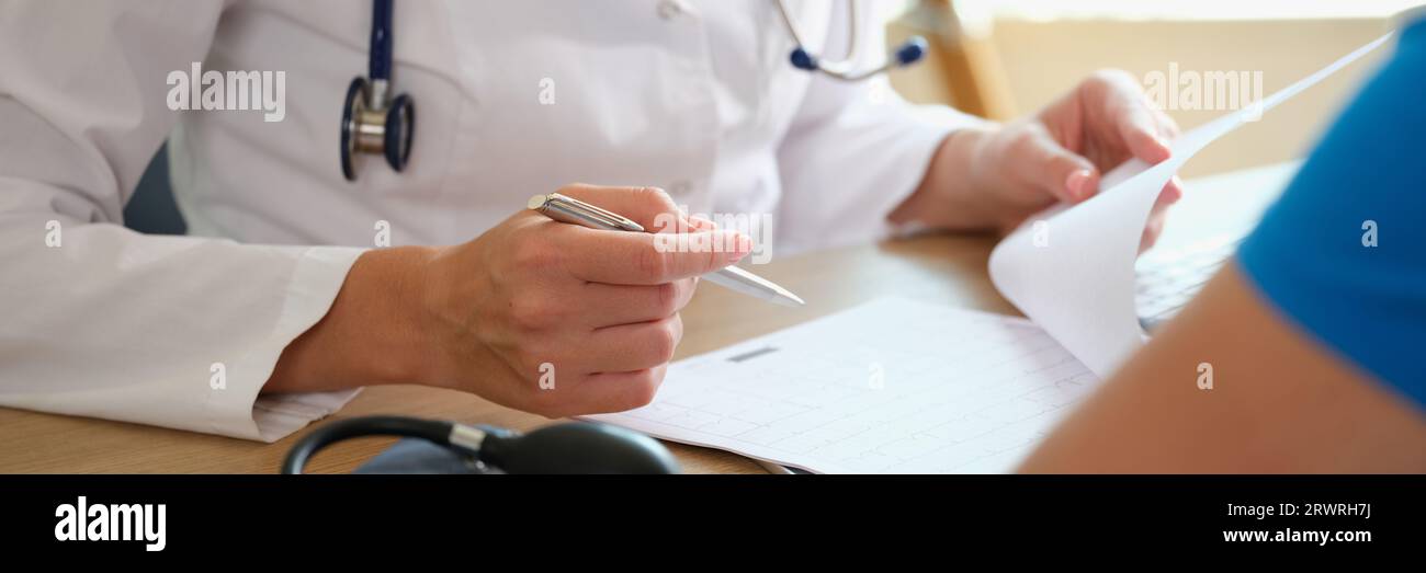 Le médecin prend des notes dans le document, assis à la table avec le patient. Banque D'Images