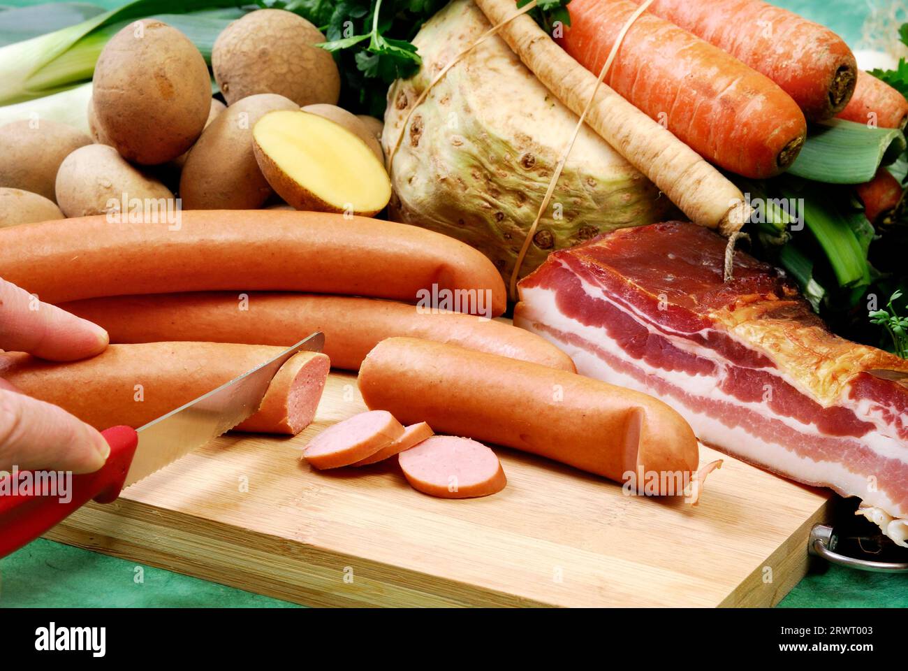 Les saucisses sont coupées sur une planche. Disposé devant des légumes frais et du bacon strié Banque D'Images