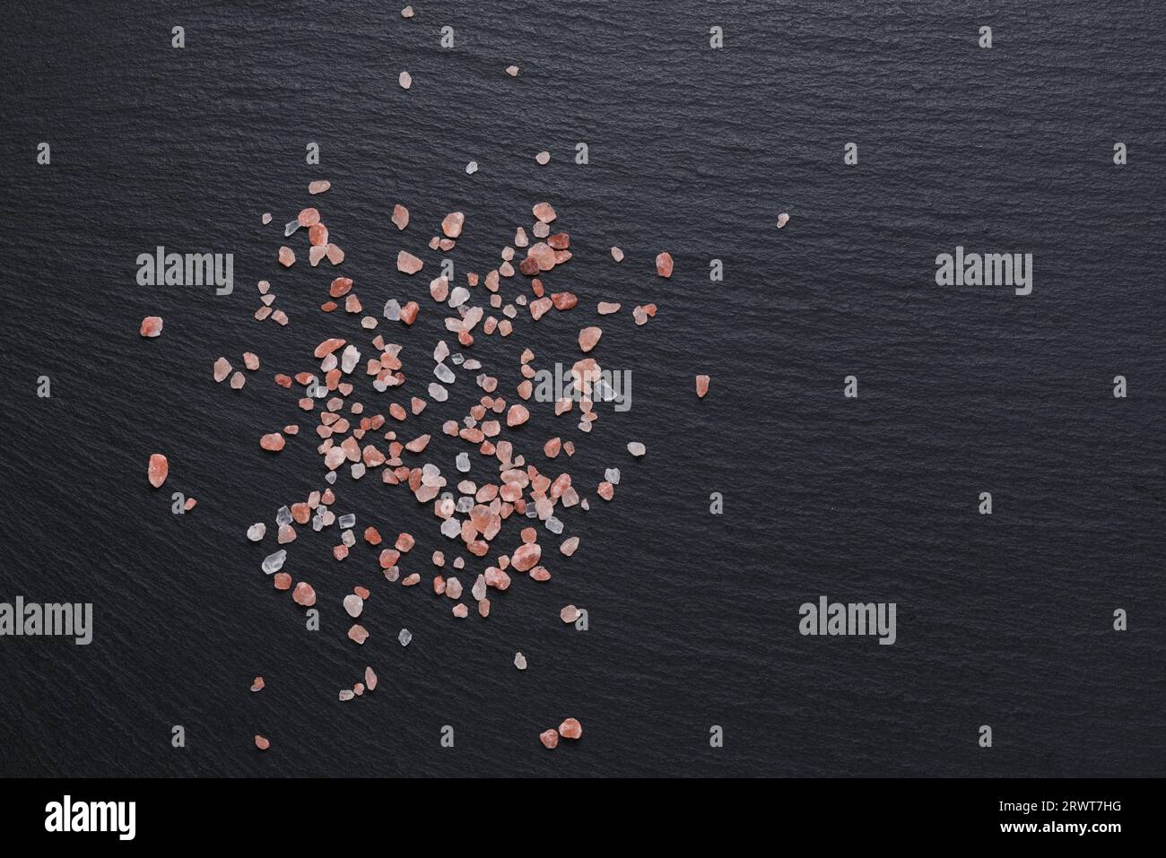 Sel rose de l'Himalaya utilisé pour les épices et les condiments en cuisine sur fond d'ardoise noire, espace de copie. Banque D'Images