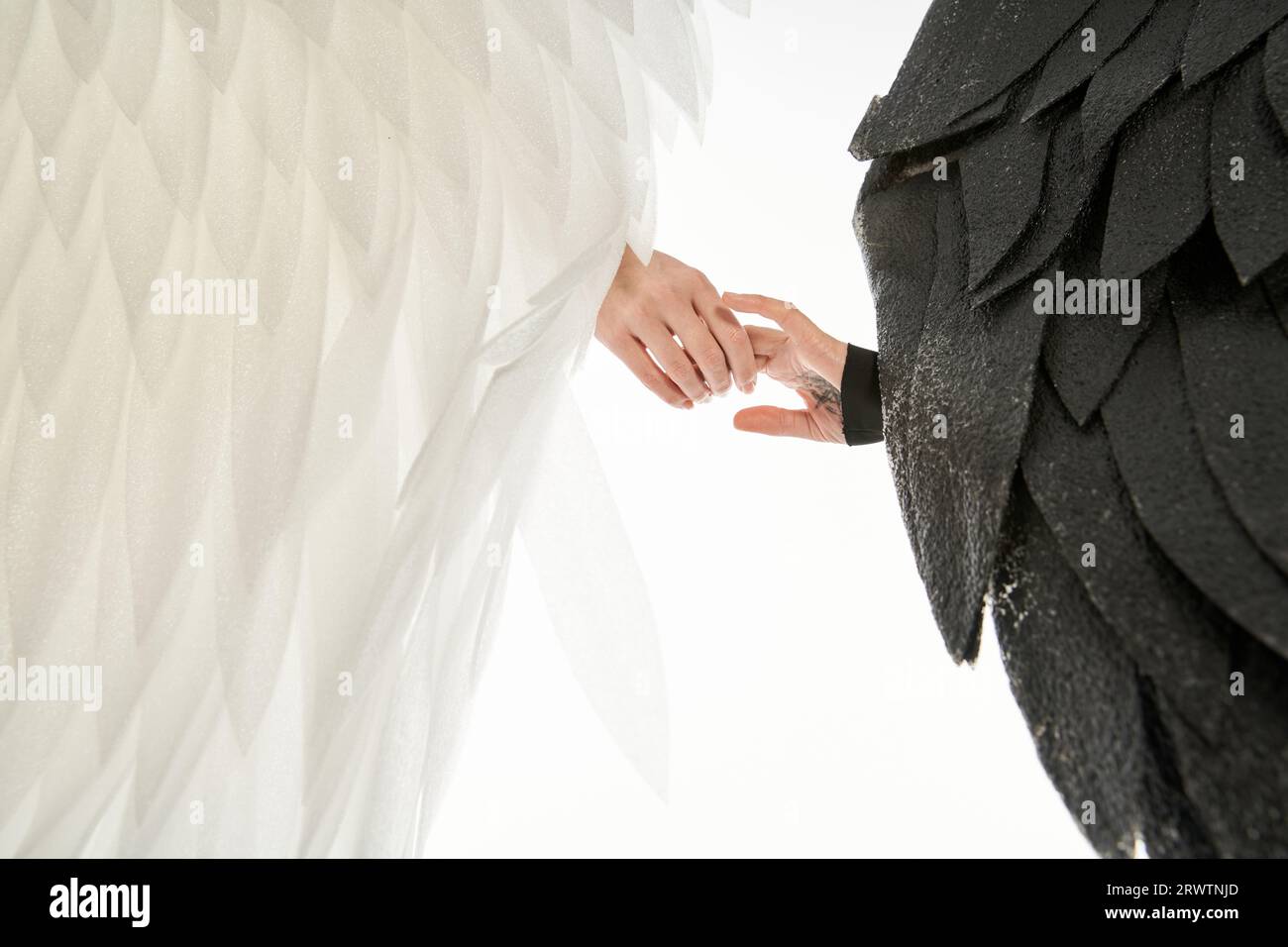 vue recadrée de l'ange et du démon avec des ailes noires et légères tenant les mains sur le blanc Banque D'Images