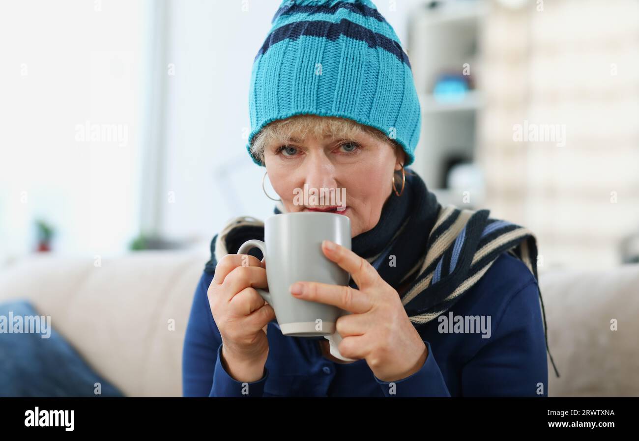 Portrait d'une femme âgée dans un chapeau chaud tenant une tasse avec des médicaments Banque D'Images