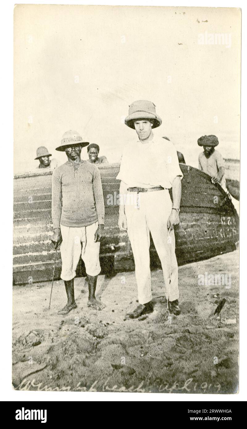 Alfred Tamlin se tient avec un ouvrier africain sur la plage de Winneba. Ils se trouvent devant un bateau à rames en bois renversé sur lequel travaillent plusieurs autres hommes. Sous-titré dans le négatif : Winnebah Beach. APL. 1919. Banque D'Images