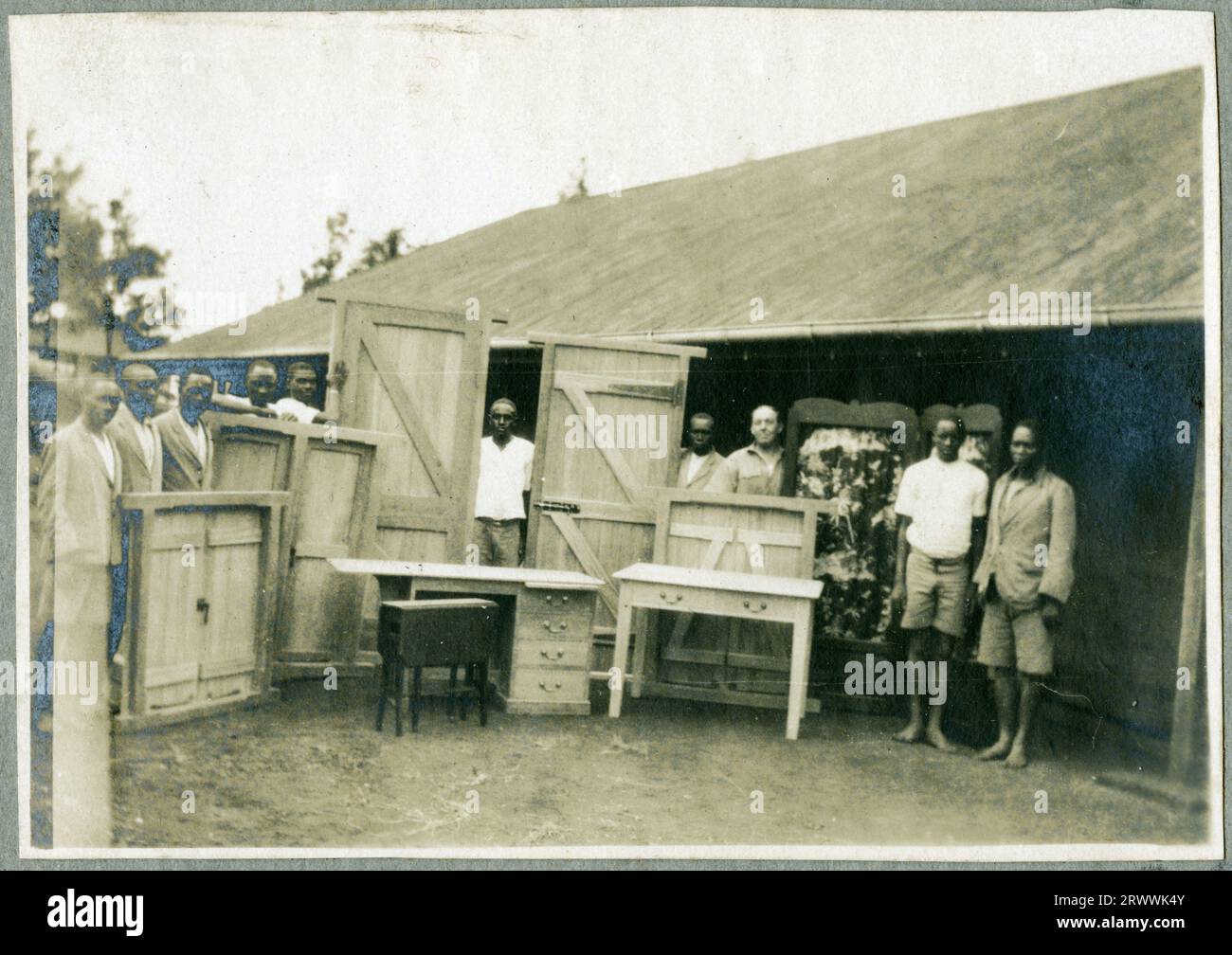 Des apprentis, probablement de l’école autochtone d’Ukamba, posent à l’extérieur de leur atelier avec leur instructeur Charles Bungey et certains de leurs produits finis en bois, y compris des portes, des écrans et des bureaux. Banque D'Images