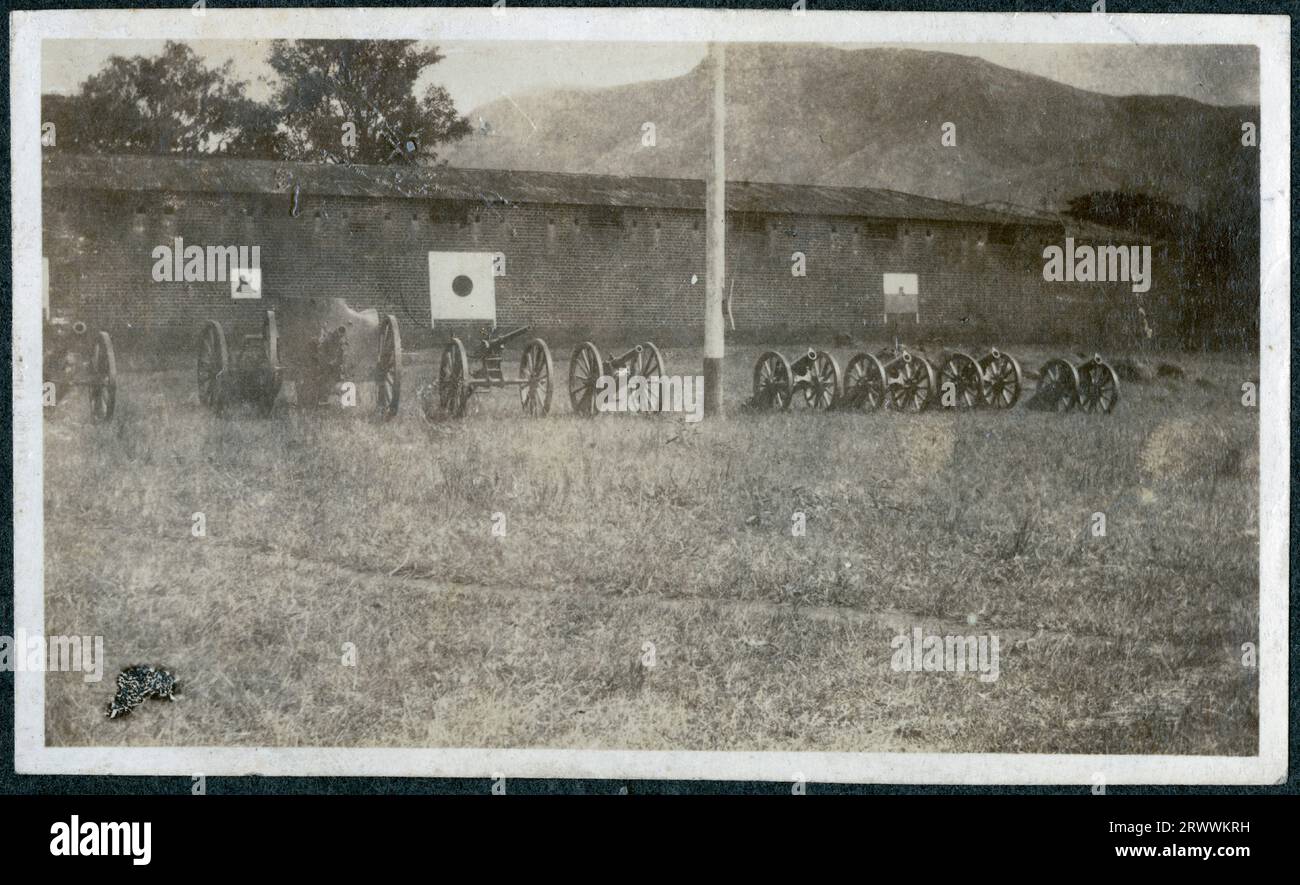 Une ligne de canons d'artillerie de différentes tailles, reposant sur des chariots de canon, sont alignés sur l'herbe à côté du haut mur d'un bâtiment du camp militaire de Zomba. Légende originale du manuscrit : quelques fusils capturés à l'extérieur du boma à Zomba, en Afrique centrale. Banque D'Images