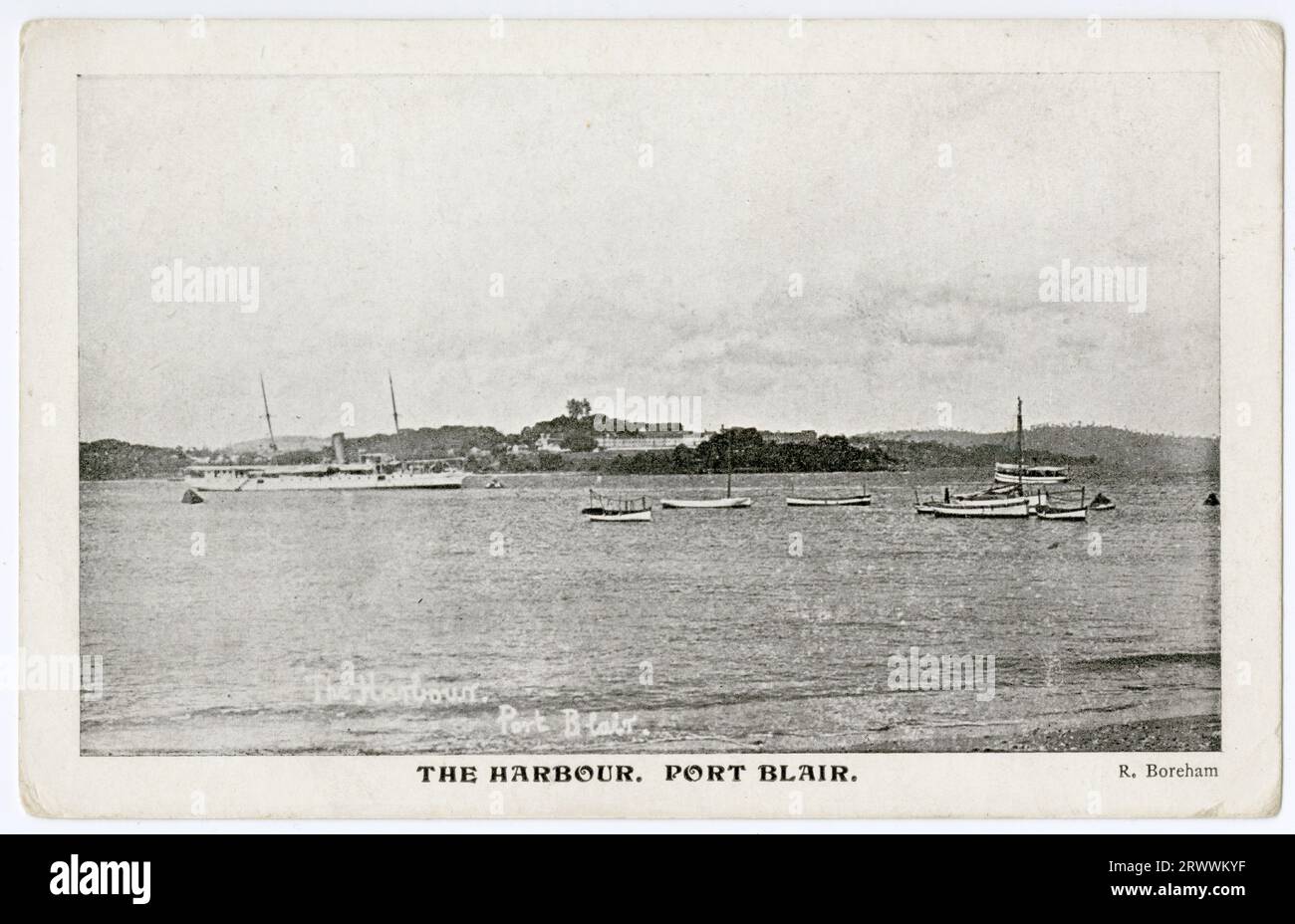 Carte postale montrant une scène de port, avec légende imprimée The Harbour, Port Blair. La légende au verso indique : c'est le port avec le R.I.M.S. 'Elphinstone' à l'ancre. J'étais le 2e ingénieur de l'Elphinstone il y a 14 ans ici. Le bâtiment que vous voyez sur le point est l'une des grandes prisons pour les prisonniers masculins. Les femelles sont dans une prison à l'autre bout du port. Banque D'Images