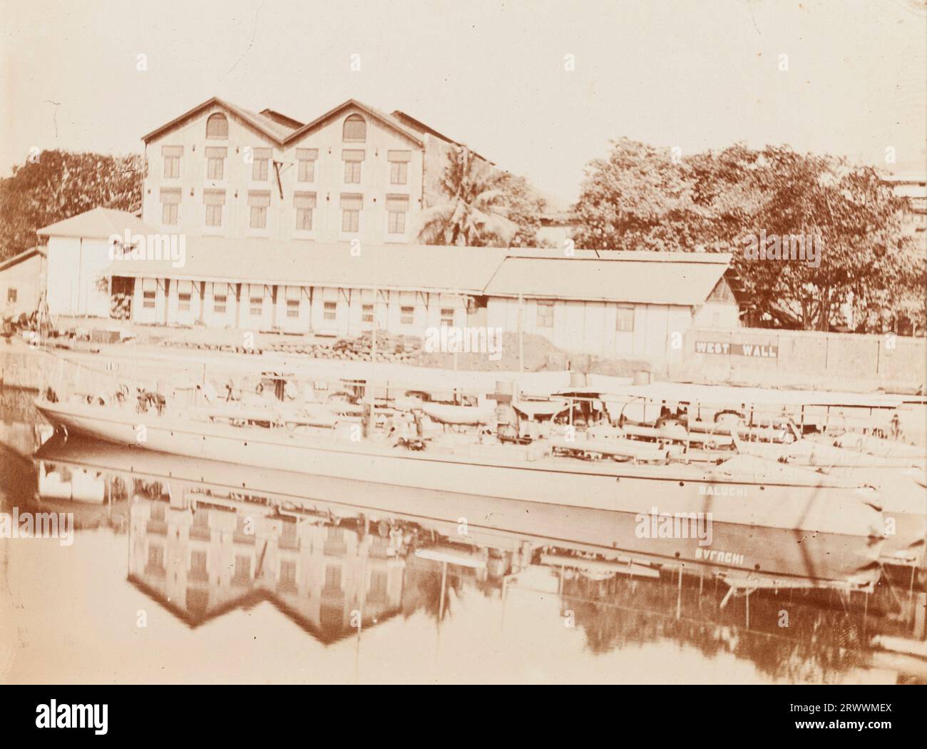 Un bateau, nommé Baluchi, est amarré au quai désigné le mur Ouest. Il y a des entrepôts avec palan et hangar de marchandises. Légende : Dockyard, Bombay. Banque D'Images