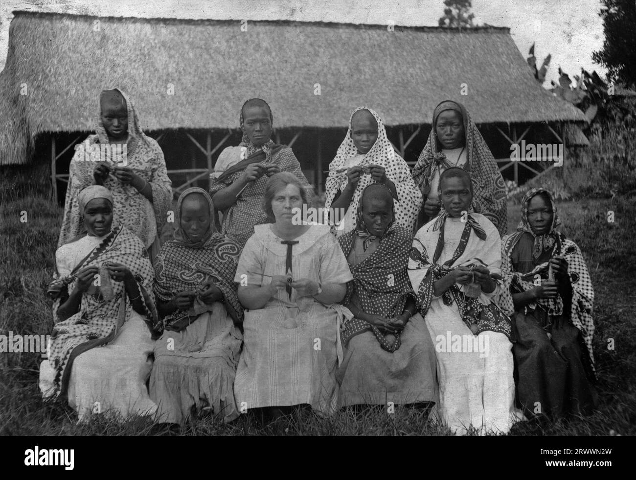 Photographie de groupe de neuf femmes africaines sur deux rangées, avec Mme Bungey au centre, devant un long bâtiment en chaume avec véranda. Les femmes tiennent des aiguilles à tricoter, des boules de laine et des travaux en cours. Une autre copie décrit l'emplacement comme Athi Plains. Banque D'Images