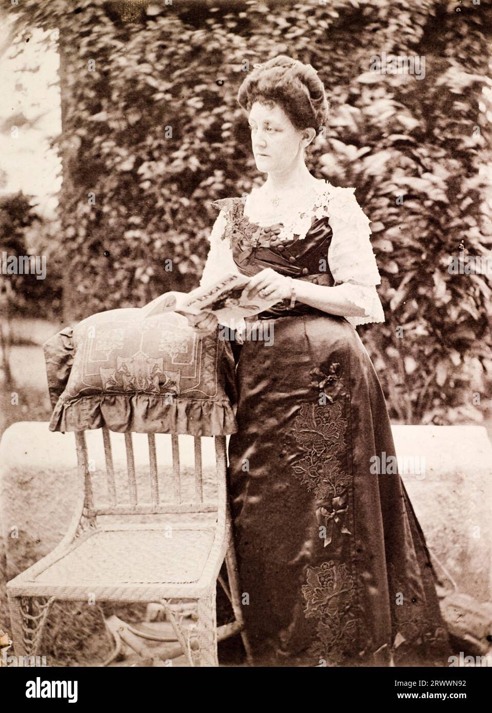 Photographie portrait de Mme Ellen Anne Wood, épouse de George Ellis Wood, prise à l'extérieur debout près d'une chaise de canne, avec un magazine ouvert dans ses mains appelé les Anglais. La légende au verso se lit comme suit : Ellen Anne Wood Andaman's 1910. Épouse de G E Wood RIM, 1907-1912 Ross Port Blair. Robe en satin noir copiée par Durzi de l'anglaise fournie par Woolands' Knightsbridge. Noir à la mort du roi Ed 7e. Banque D'Images