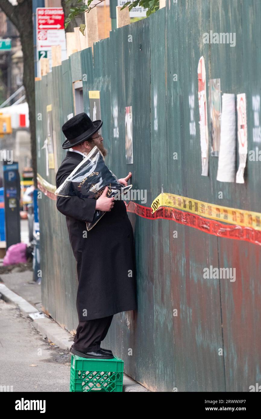 Sur un chantier de construction à Brooklyn, un juif orthodoxe ne peut résister à regarder la construction en cours à travers un trou. À Brooklyn, New York. Banque D'Images