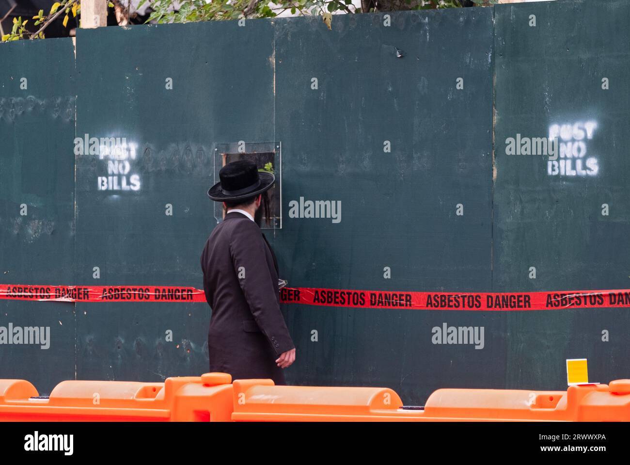 Sur un chantier de construction à Brooklyn, un juif orthodoxe ne peut résister à regarder la construction en cours à travers un trou. À Brooklyn, New York. Banque D'Images