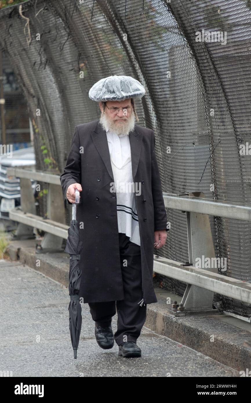 Un homme juif plus âgé marche pendant une légère bruine portant un chapeau de pluie fait maison. Sur Lee Avenue à Williamsburg, Brooklyn, New York. Banque D'Images