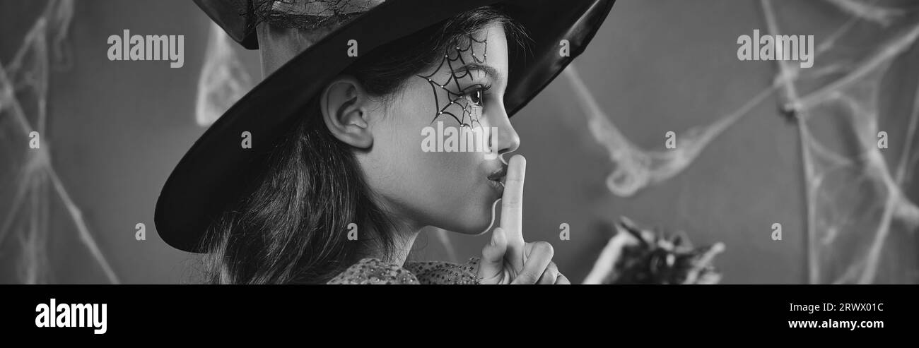 Jolie petite fille en costume de sorcière Halloween et chapeau pointu montrant shh bannière noire et blanche Banque D'Images