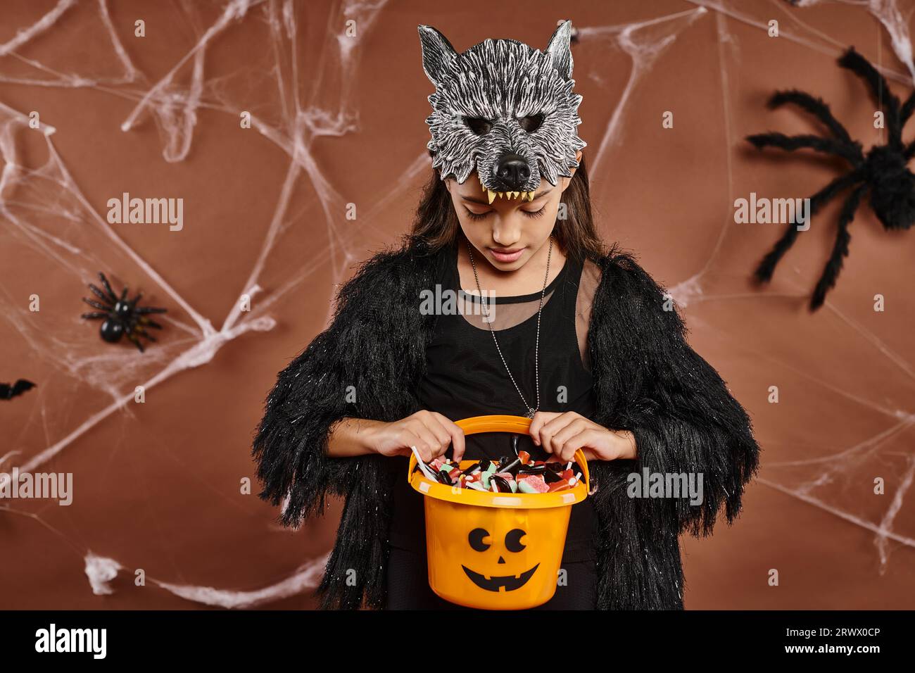 Close up fille preteen regardant son seau de bonbons sur fond brun avec toile d'araignée, Halloween Banque D'Images
