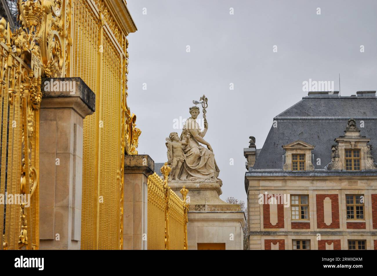 Une statue d'Hermès avec une mouette sur la tête, tenant le caducée, à l'extérieur du château de Versailles clôturé par des portes dorées ornées Banque D'Images