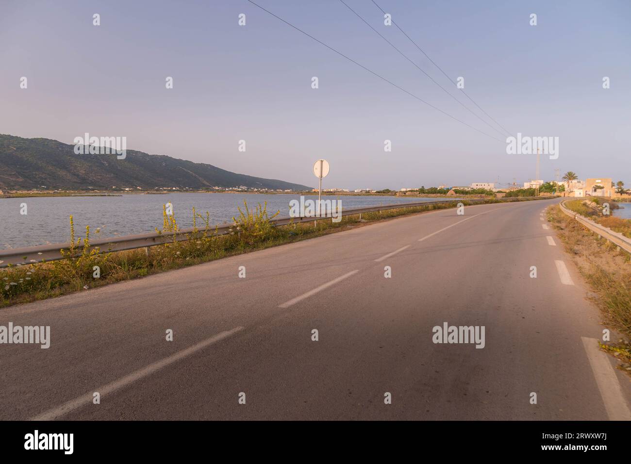 La route dans le Ghar El Melh, Tunisie, longeant la rive du lac pendant le coucher du soleil. Banque D'Images