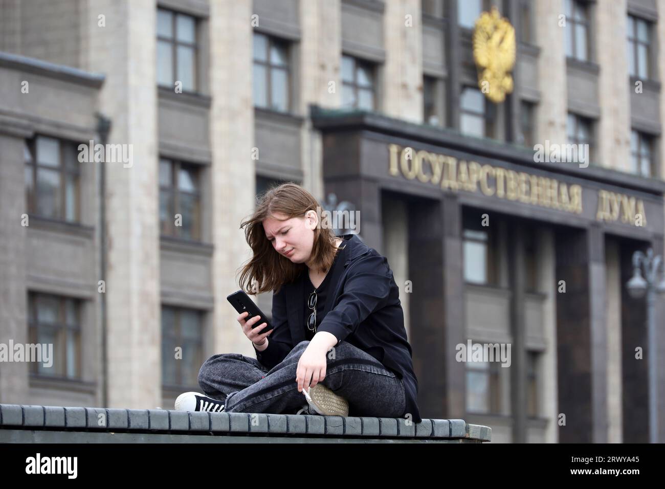 Fille assise avec un smartphone sur le banc contre la Douma d'État à Moscou Banque D'Images