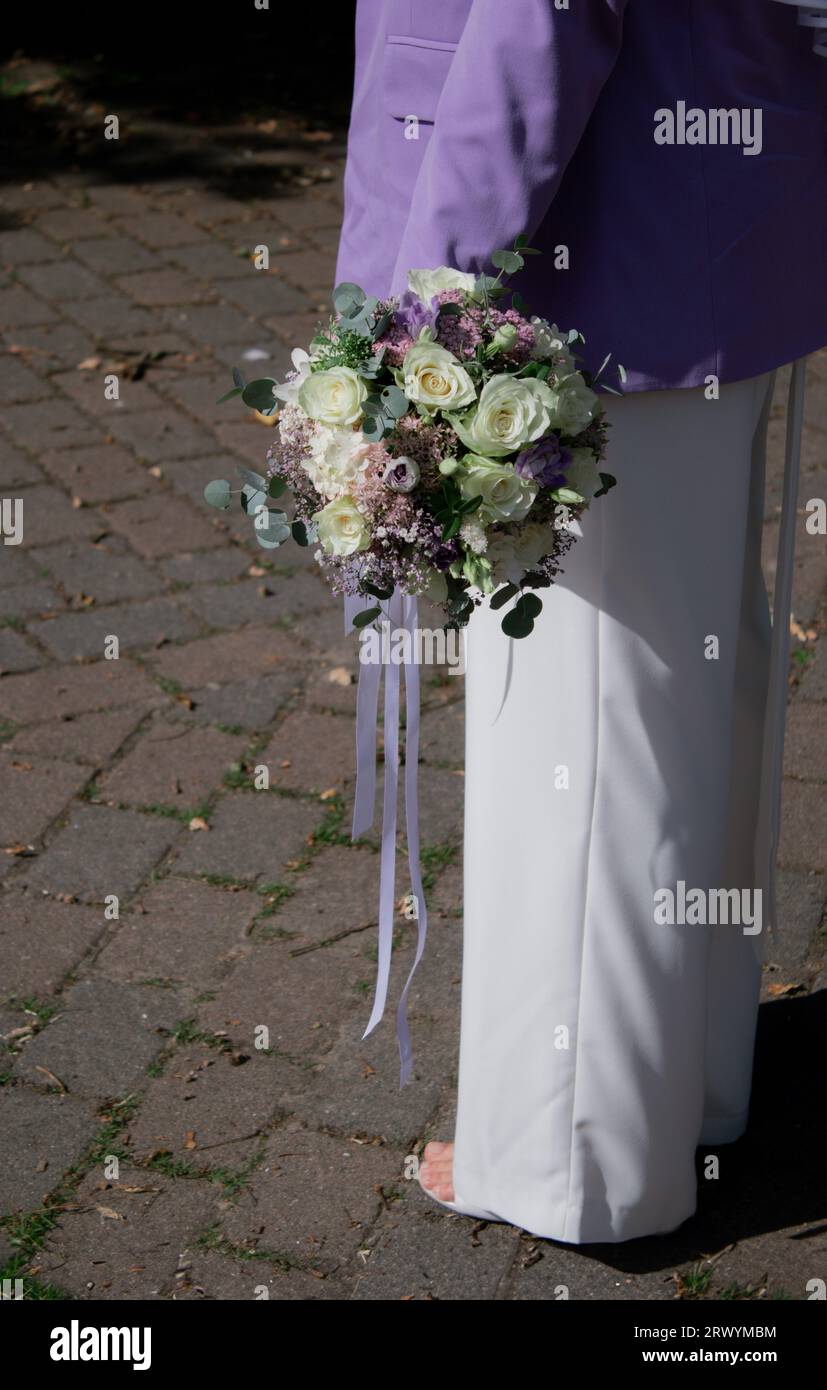Gros plan de mariée moderne tenant un bouquet de mariage avec des fleurs blanches et violettes Banque D'Images