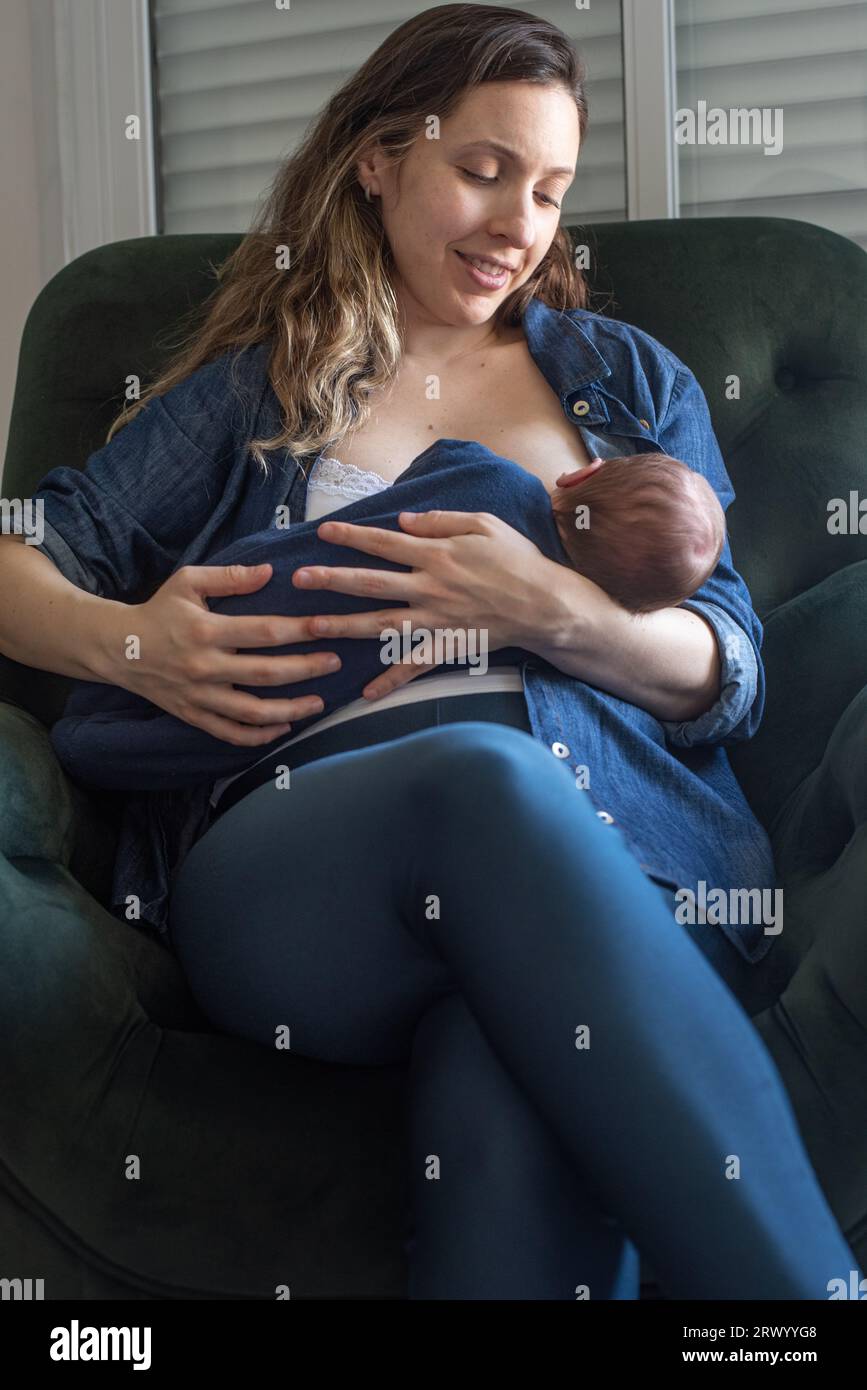 Mère heureuse allaitant son bébé fils assis sur un fauteuil à la maison Banque D'Images