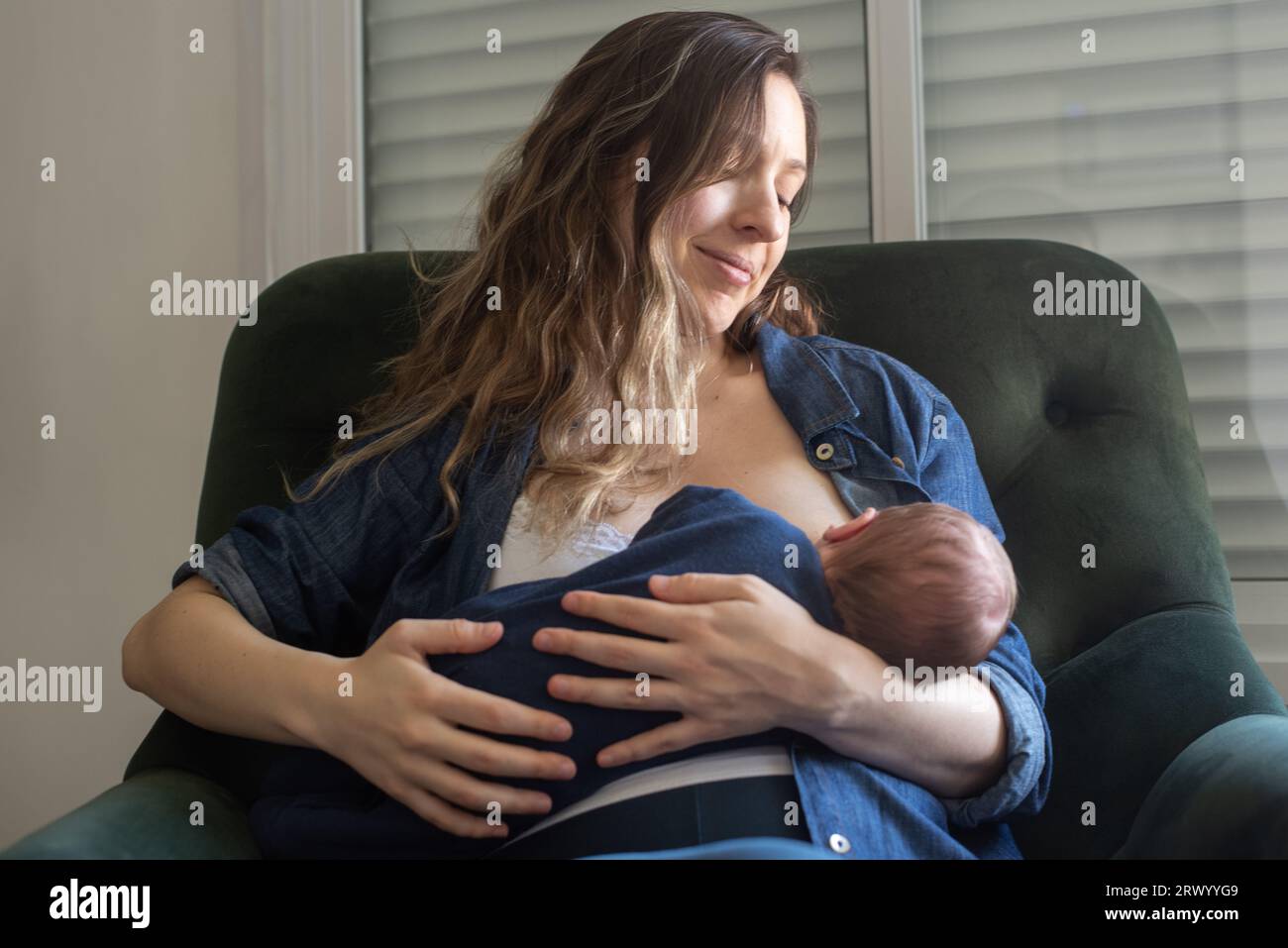 Mère heureuse allaitant son bébé fils assis sur un fauteuil à la maison Banque D'Images