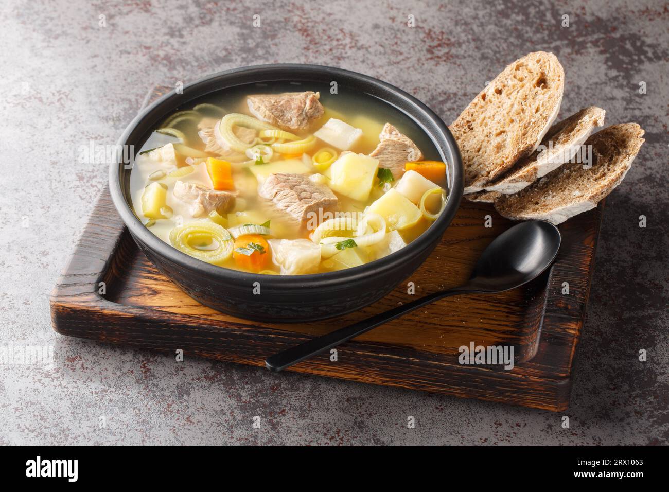 Soupe aromatique de légumes racines avec du bœuf servi avec du pain de seigle en gros plan dans un bol sur la table. Horizontal Banque D'Images