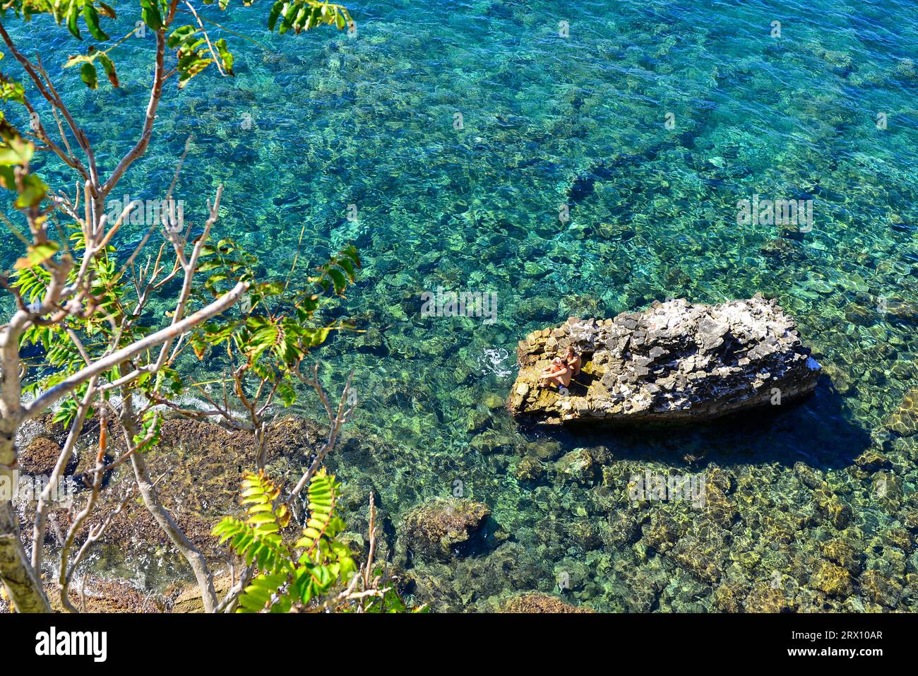 Bathers Chillin' sur un rocher juste à côté de Budva Citadelle, Monténégro, sur une journée ensoleillée fin septembre 2013. Roches submergées dans les eaux aigue-marine visibles Banque D'Images