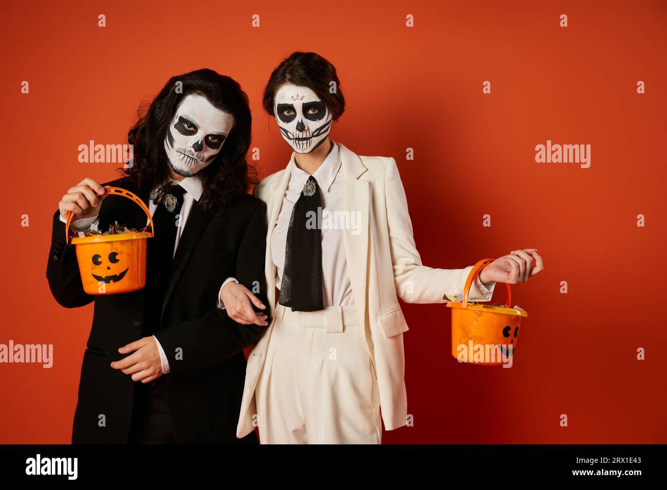 couple élégant en dia de los muertos maquillage tenant des seaux de bonbons et regardant la caméra sur le rouge Banque D'Images