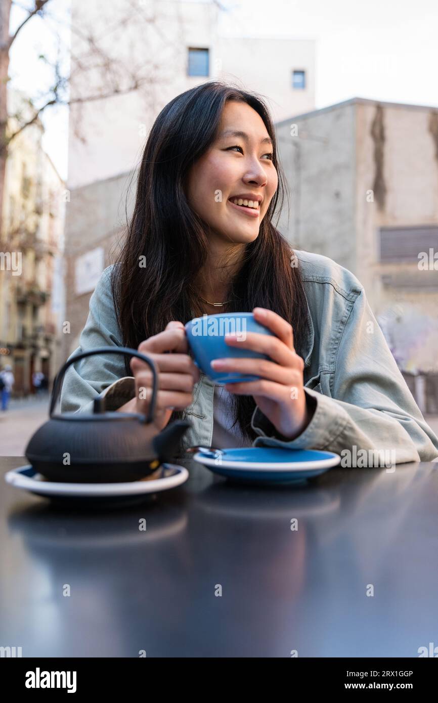 Joyeuse femme heureuse buvant une tasse de thé dans une terrasse de bar. Banque D'Images