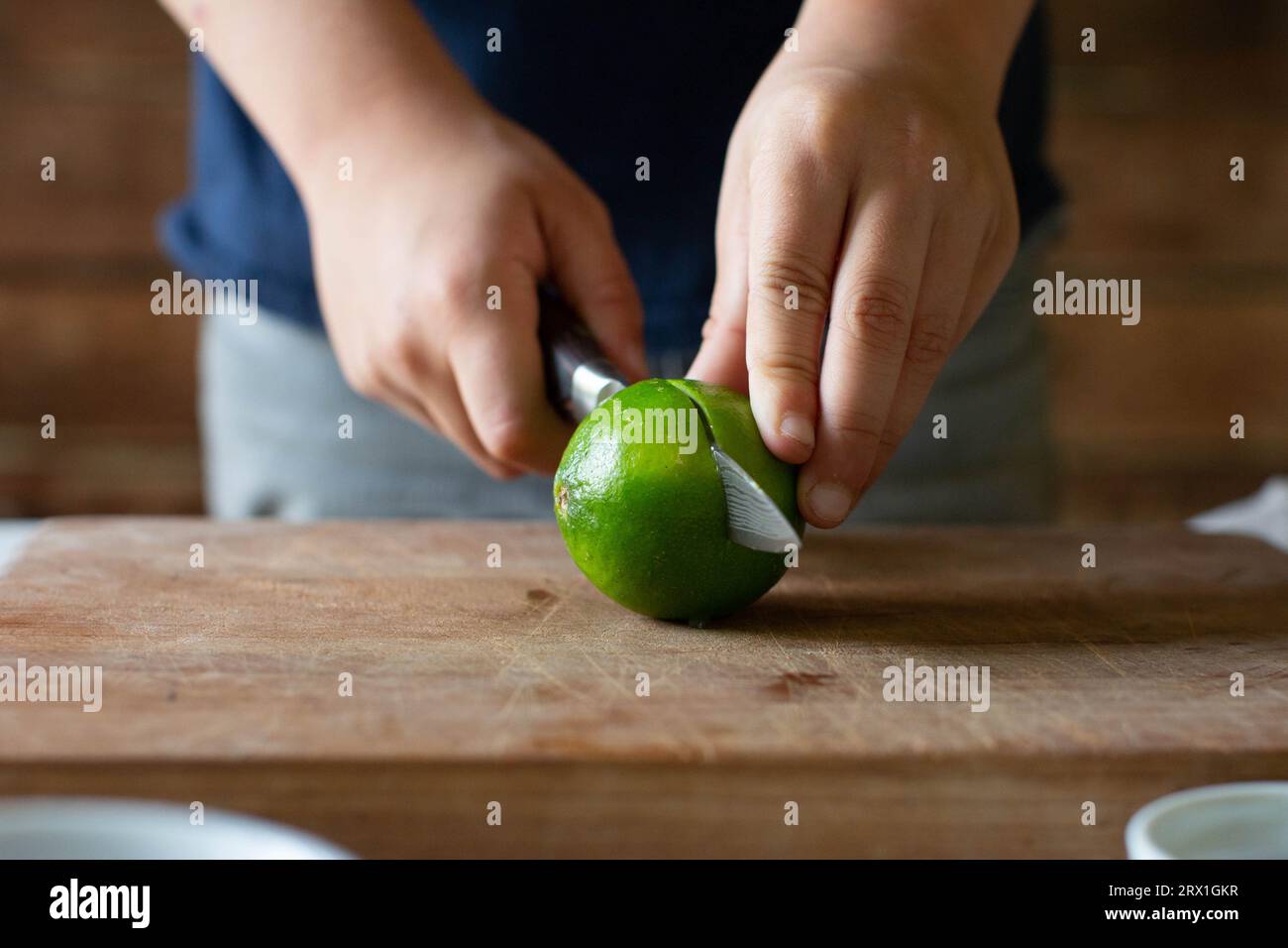 Garçon en chemise bleue utilisant un couteau pour trancher le citron vert Banque D'Images