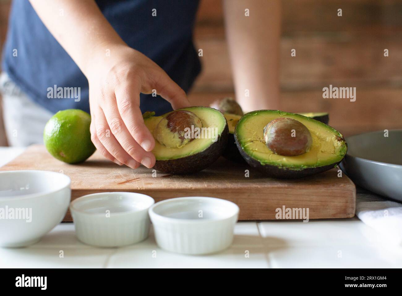 Garçon en chemise bleue tenant Avacados sur la planche à découper Banque D'Images