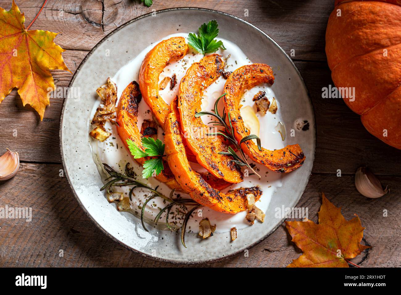 Citrouille grillée avec du fromage grec et des herbes sur fond rustique en bois. Salade de citrouille épicée chaude d'hiver avec yaourt. Banque D'Images