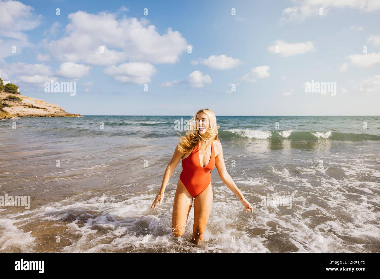 Femme souriante en maillot de bain marchant hors de l'eau de mer à la plage Banque D'Images