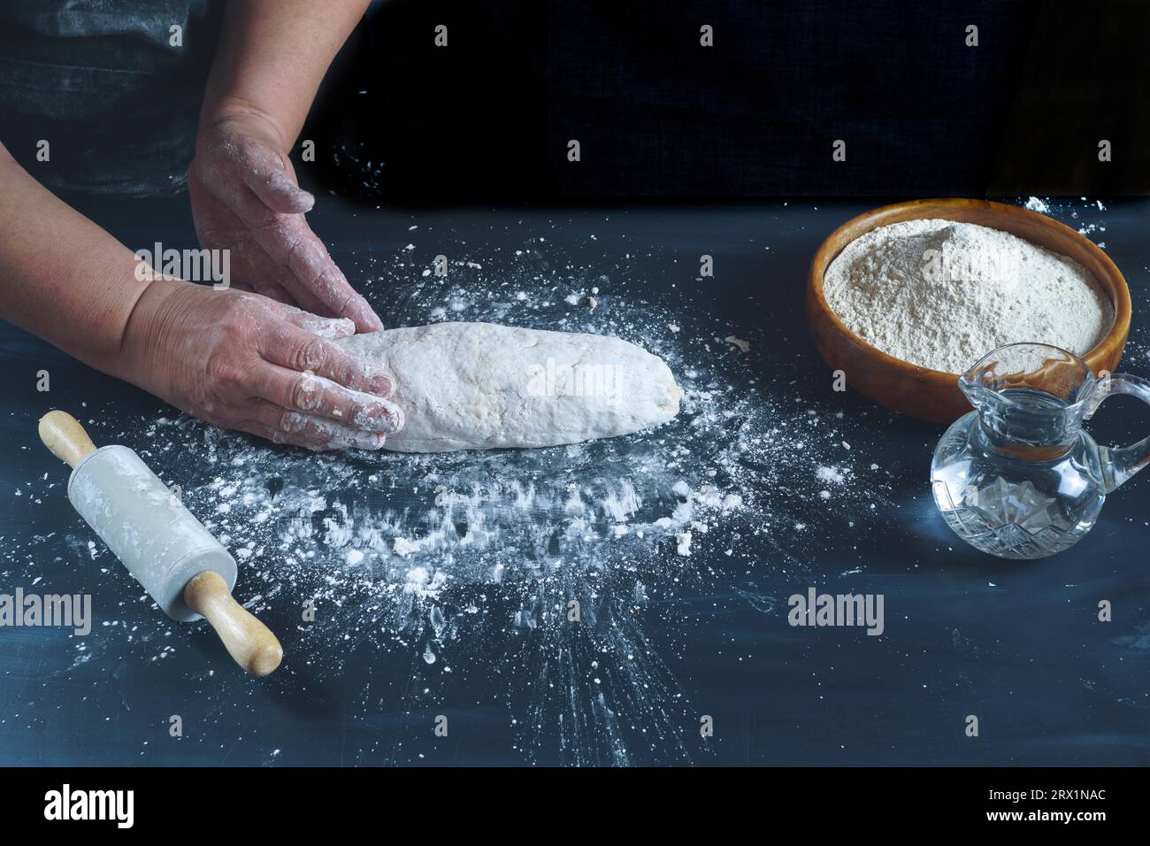 Femme pétrissant avec ses mains une pâte à farine pour faire du pain maison sur une table en bois noir avec de la farine, de l'eau et un rouleau à pâtisserie Banque D'Images