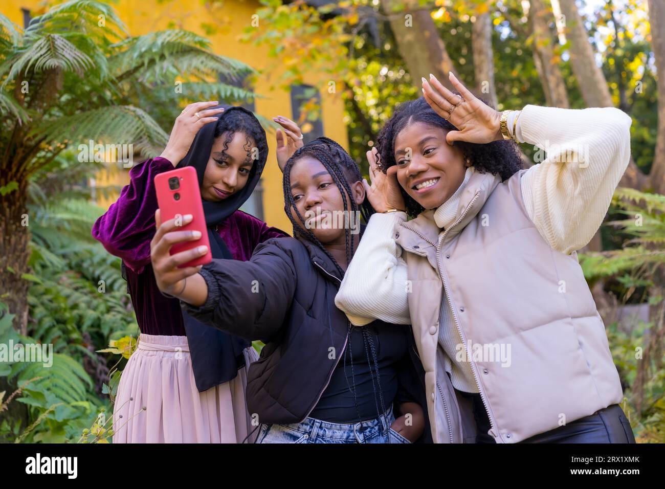 Amis africains et musulmans drôles grimaceant et faisant des gestes tout en prenant un selfie debout dans un parc urbain Banque D'Images