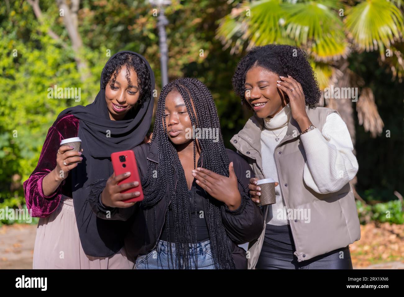 Des jeunes femmes africaines et une amie musulmane prenant un selfie dans un parc Banque D'Images